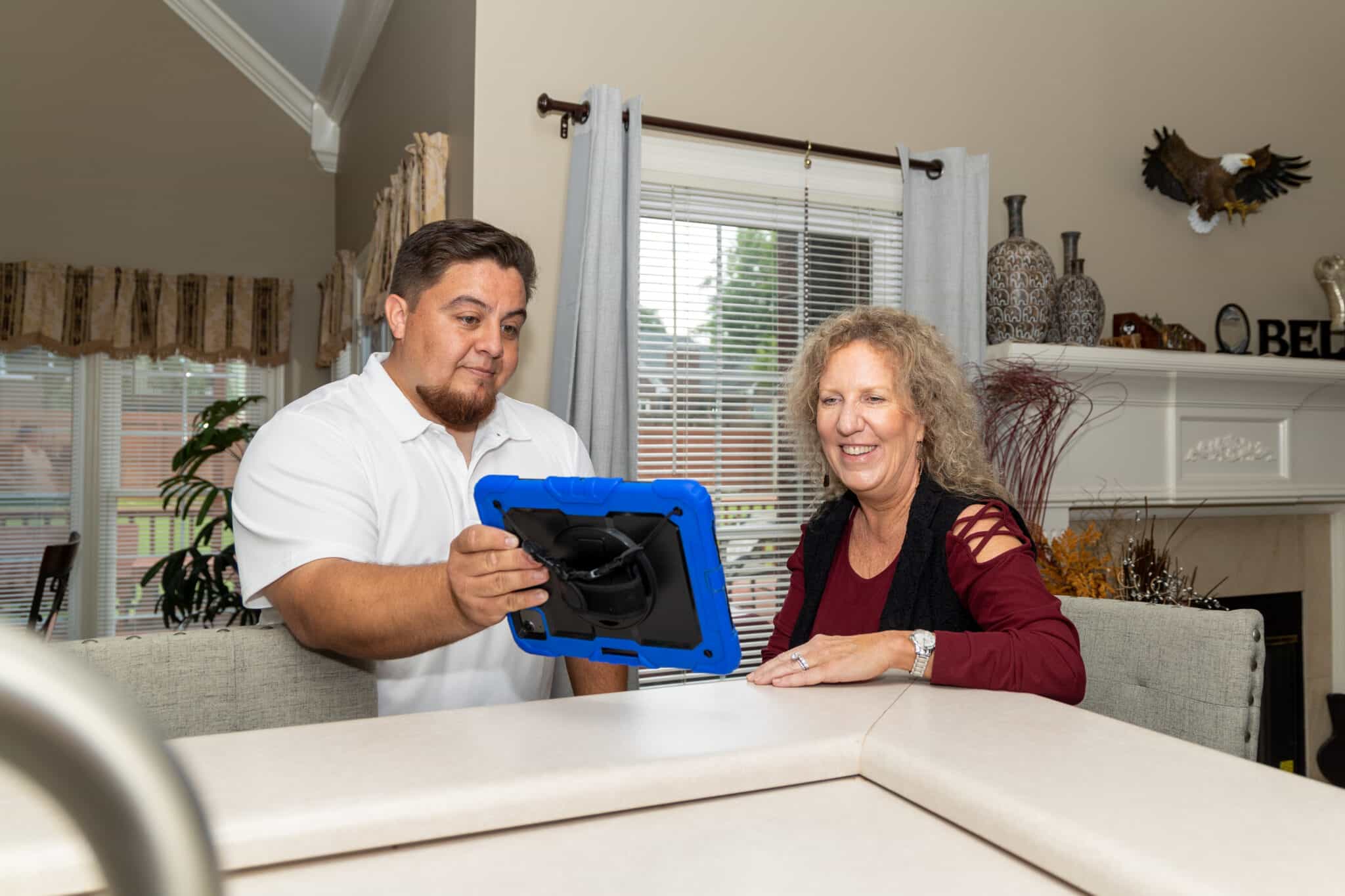 Aire Solutions technician shows a customer information about a geothermal HVAC system on a tablet during an in-home consultation.