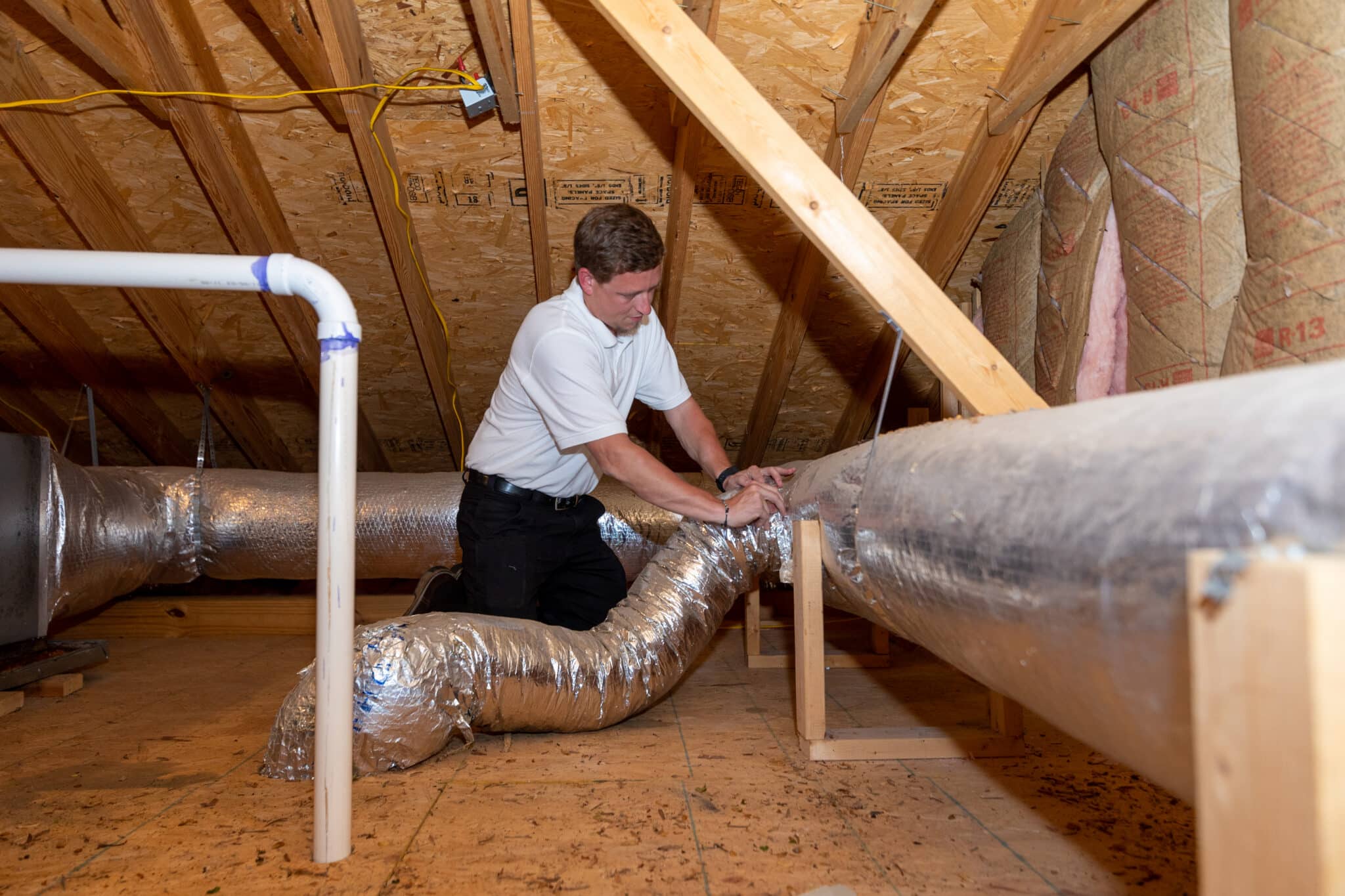 Technician inspecting and sealing air ducts in an attic